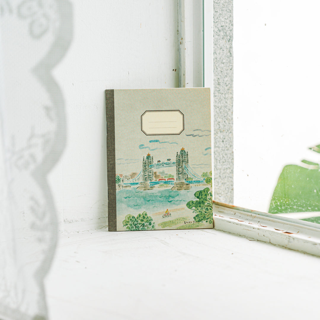 Notebook with a scenic cover design on a white surface near a window