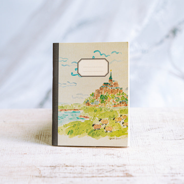 Notebook with a colorful illustration of a village on a hillside against a white background