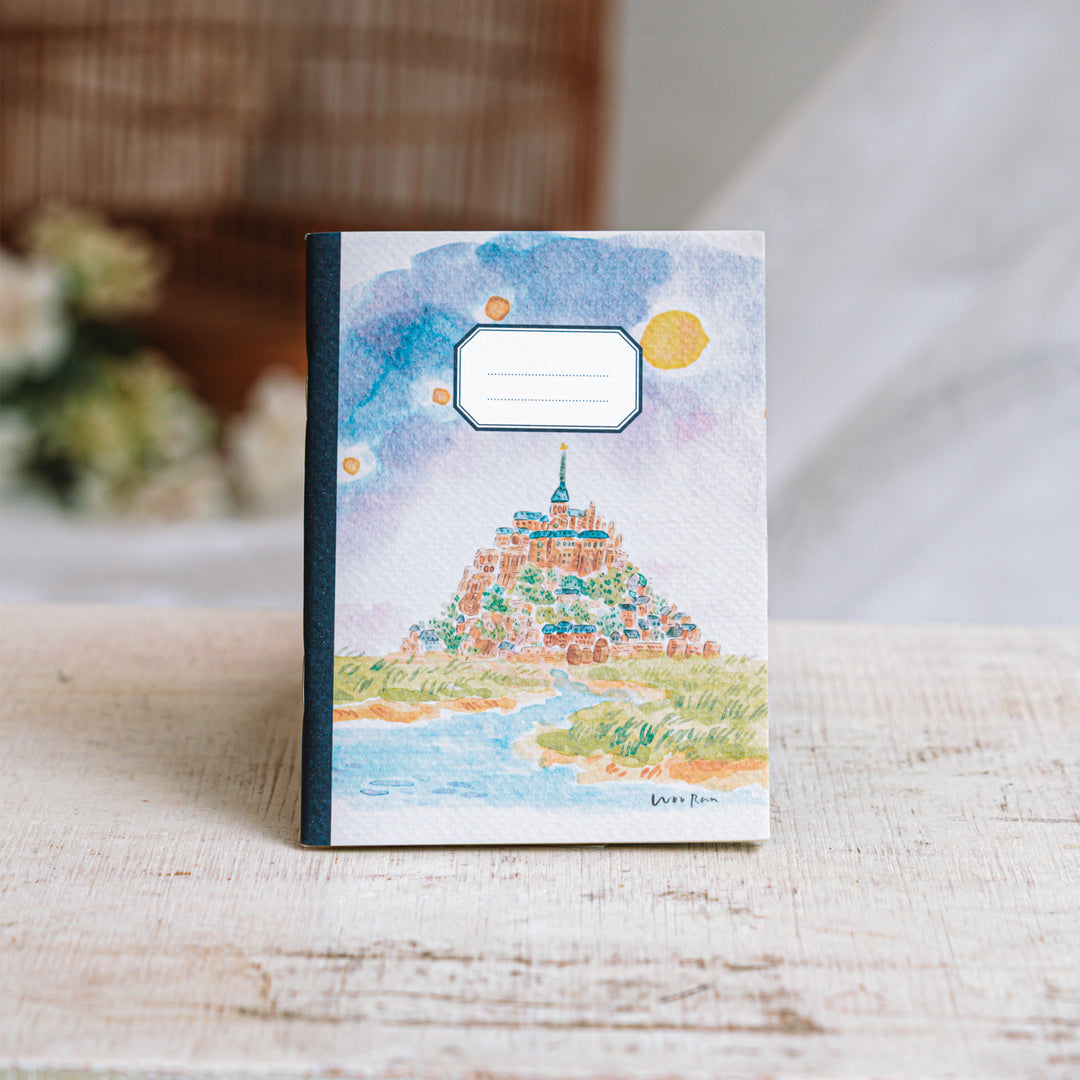 Notebook with a colorful illustration of a mountain and sky on a wooden surface.