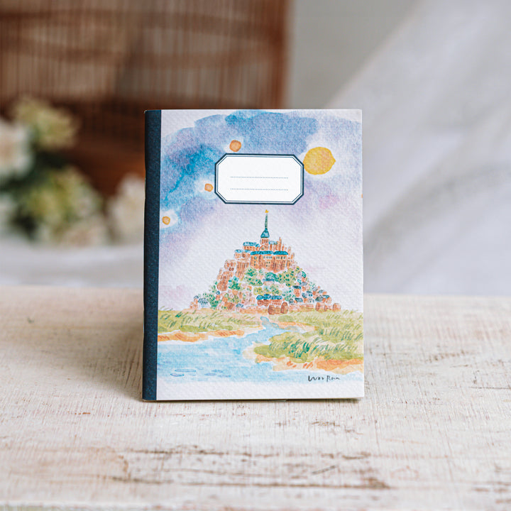 Notebook with a colorful illustration of a mountain and sky on a wooden surface.