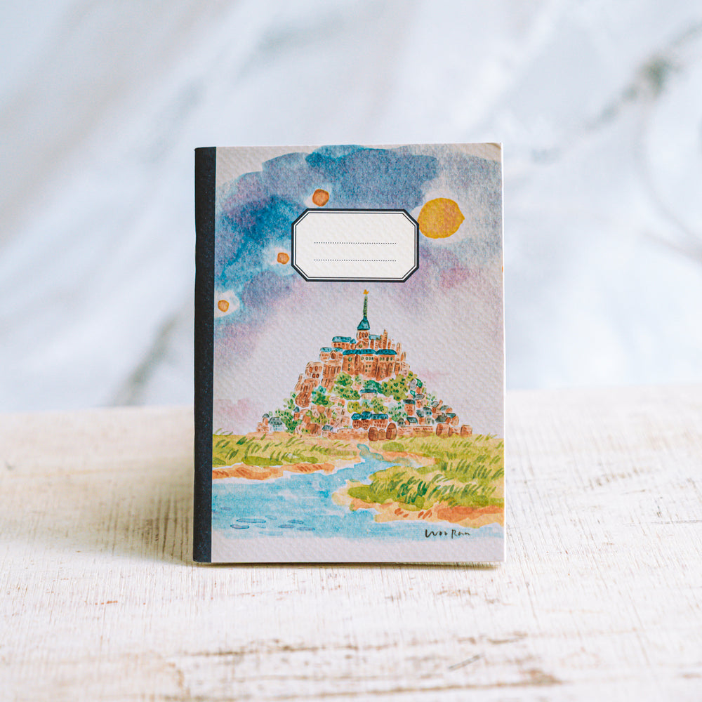 Notebook with a colorful illustration of a castle on a hill against a sunset.