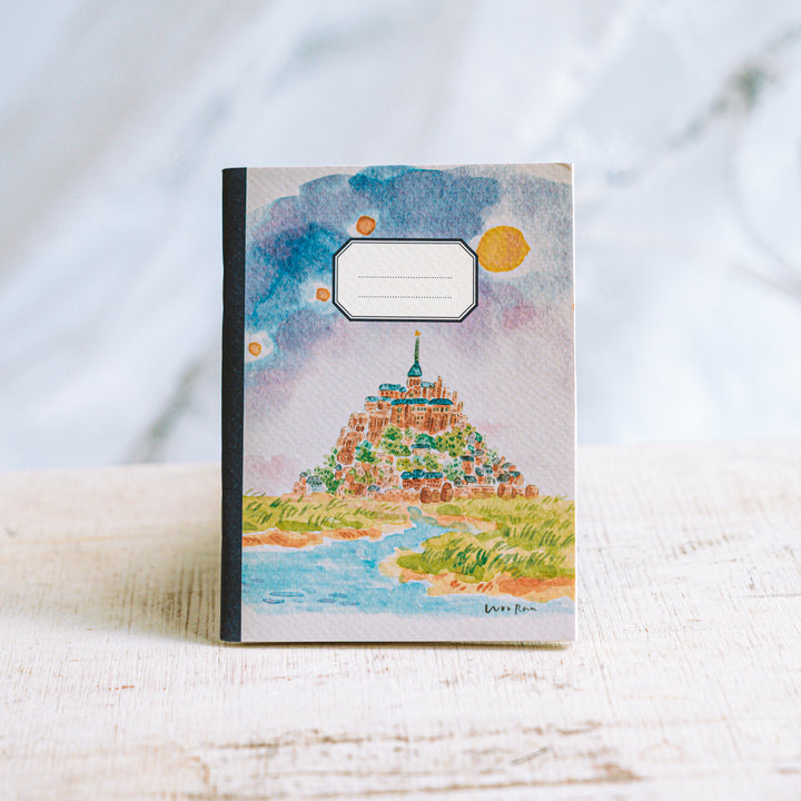 Notebook with a colorful illustration of a castle on a hill against a sunset.