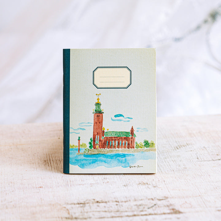 Notebook with a watercolor illustration of a building on a white surface