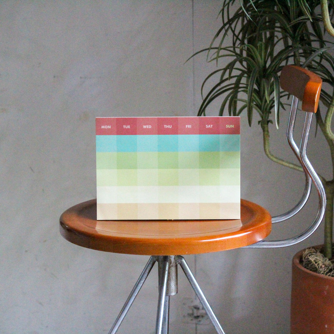 Monthly planner with colorful blocks on a wooden stool with a plant in the background